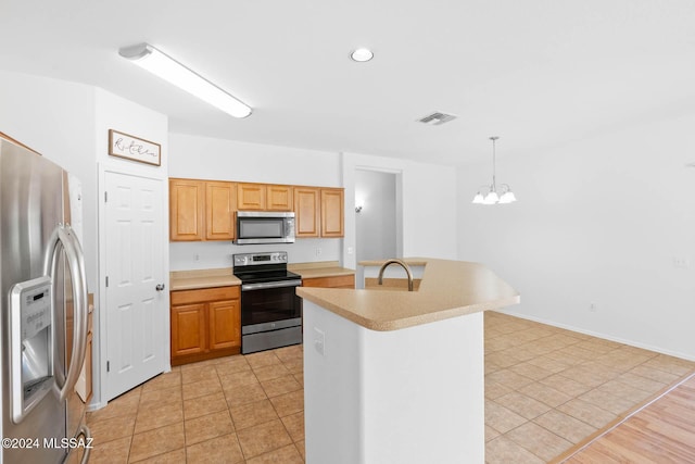 kitchen featuring sink, stainless steel appliances, a chandelier, pendant lighting, and a kitchen island with sink