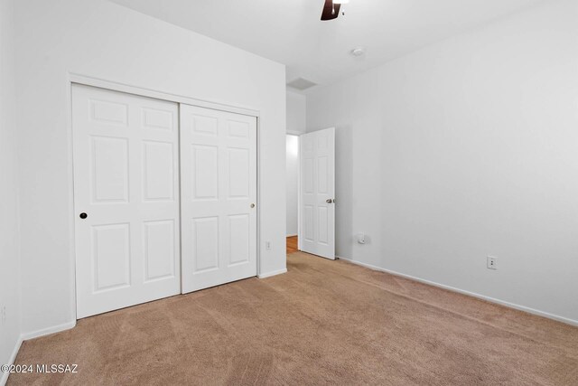 unfurnished bedroom with ceiling fan, light carpet, and a closet