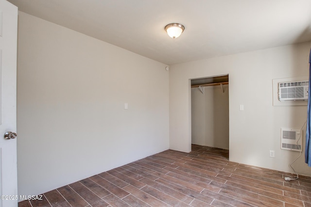 unfurnished bedroom featuring heating unit, a closet, wood-type flooring, and an AC wall unit