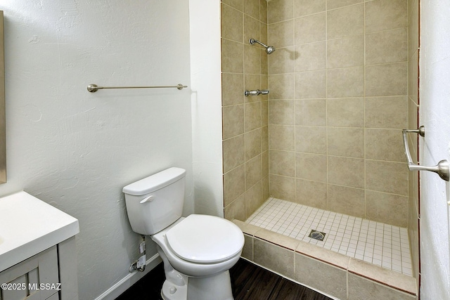 bathroom with hardwood / wood-style flooring, tiled shower, vanity, and toilet