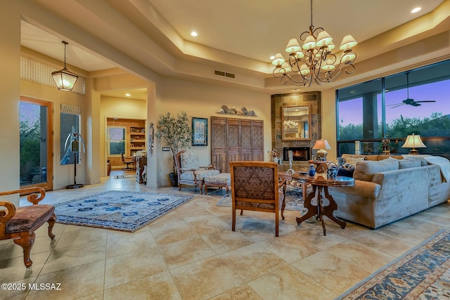 living room with a fireplace, ceiling fan with notable chandelier, a high ceiling, and a tray ceiling