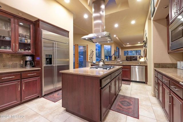 kitchen with light tile patterned floors, island range hood, built in appliances, and a kitchen island