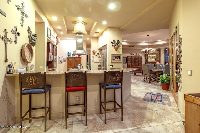 kitchen featuring island exhaust hood, a kitchen breakfast bar, kitchen peninsula, a chandelier, and a tray ceiling