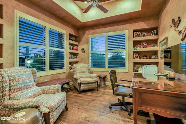 home office with ceiling fan, built in features, hardwood / wood-style flooring, and a tray ceiling