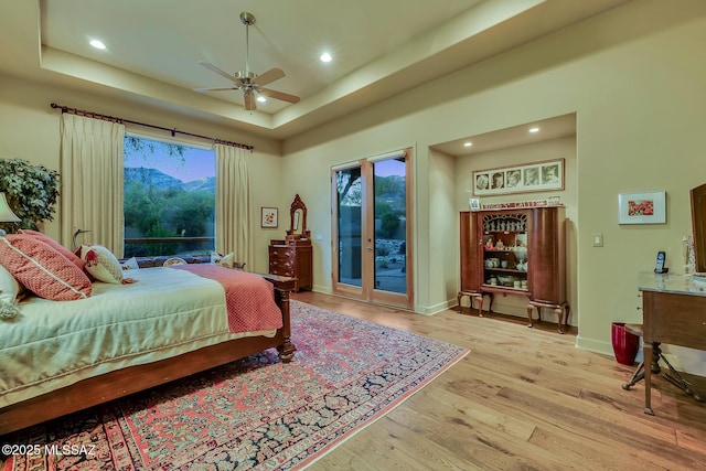 bedroom featuring a mountain view, ceiling fan, a raised ceiling, access to outside, and light hardwood / wood-style flooring