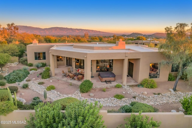 back house at dusk featuring a patio area, a mountain view, and a hot tub