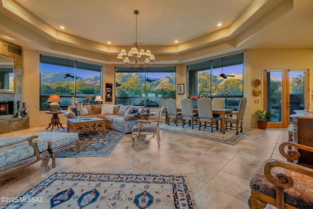 living room featuring a raised ceiling, a high ceiling, a mountain view, and ceiling fan with notable chandelier