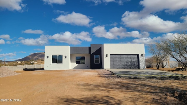 contemporary home with a mountain view, a garage, fence, concrete driveway, and stucco siding