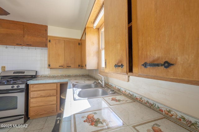 kitchen with tile countertops, decorative backsplash, gas stove, light tile patterned flooring, and sink