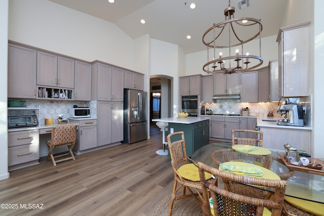 kitchen with gray cabinets, appliances with stainless steel finishes, decorative backsplash, high vaulted ceiling, and a kitchen island