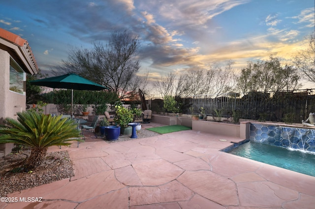 pool at dusk with pool water feature and a patio