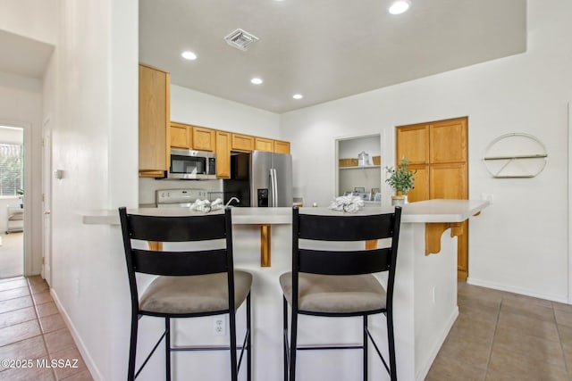 kitchen featuring stainless steel appliances, a breakfast bar, dark tile patterned flooring, and kitchen peninsula