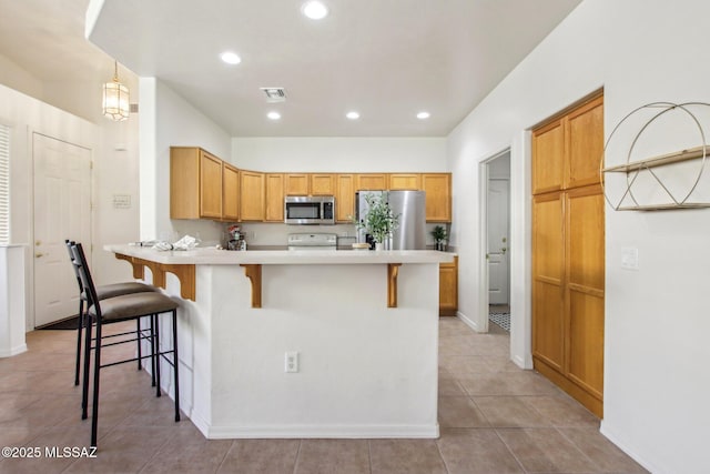 kitchen with decorative light fixtures, light tile patterned floors, appliances with stainless steel finishes, a kitchen breakfast bar, and kitchen peninsula