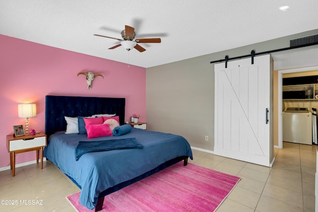 bedroom with tile patterned floors, ceiling fan, a barn door, a textured ceiling, and washer / dryer