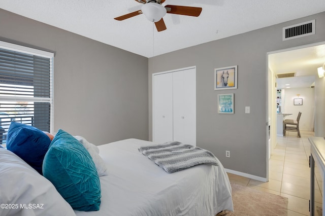 bedroom featuring a textured ceiling, a closet, ceiling fan, and light tile patterned flooring