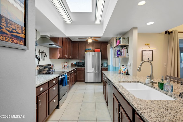 kitchen with light stone counters, wall chimney exhaust hood, stainless steel appliances, sink, and light tile patterned floors