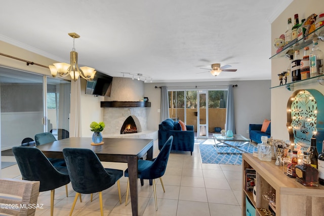 tiled dining area with a fireplace, rail lighting, ceiling fan with notable chandelier, and ornamental molding