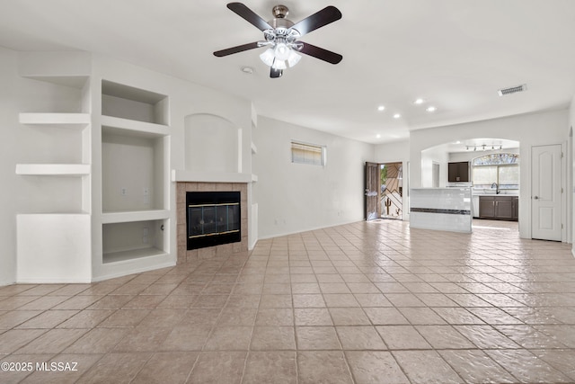 unfurnished living room featuring a tile fireplace, ceiling fan, sink, built in features, and light tile patterned flooring