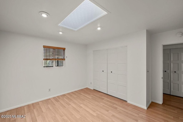 unfurnished bedroom featuring a skylight, light hardwood / wood-style floors, and a closet