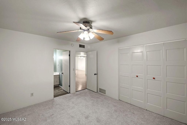 unfurnished bedroom featuring carpet flooring, ensuite bath, ceiling fan, and a closet