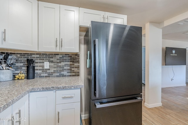 kitchen with white cabinets, backsplash, light stone counters, and stainless steel refrigerator