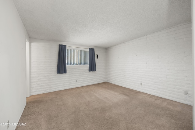 empty room with carpet floors, a textured ceiling, and brick wall