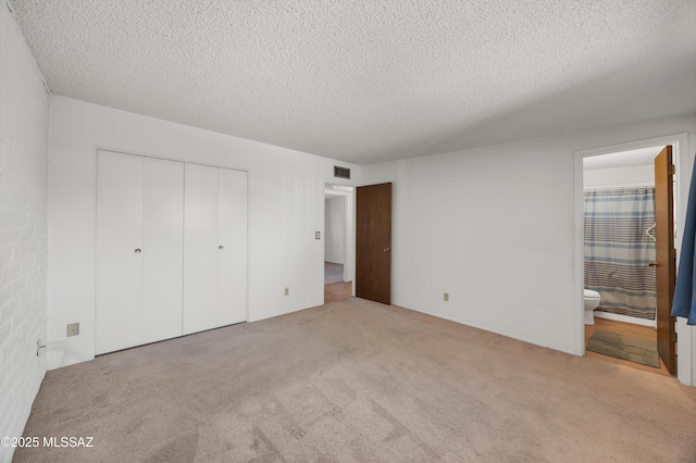 unfurnished bedroom with ensuite bathroom, light carpet, a textured ceiling, and a closet