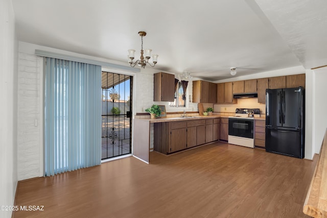 kitchen with under cabinet range hood, range with electric stovetop, wood finished floors, light countertops, and freestanding refrigerator