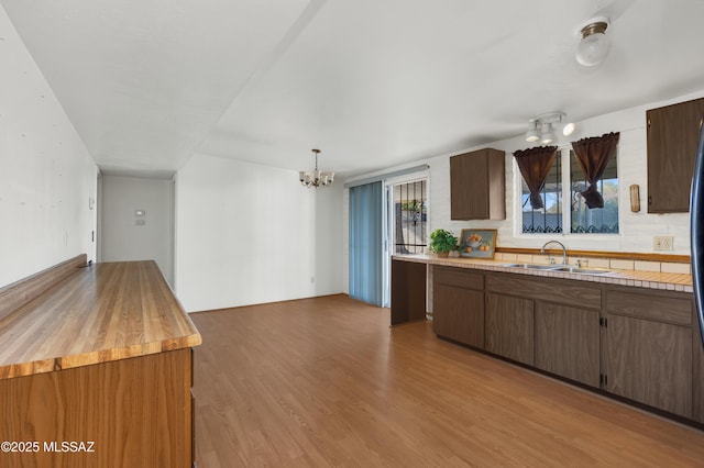 kitchen featuring a notable chandelier, hanging light fixtures, backsplash, a sink, and light wood-type flooring