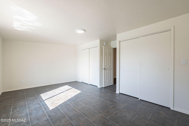 unfurnished bedroom with two closets and dark tile patterned flooring