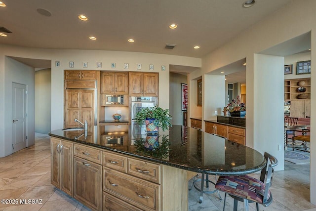 kitchen with sink, a kitchen island with sink, dark stone counters, and appliances with stainless steel finishes