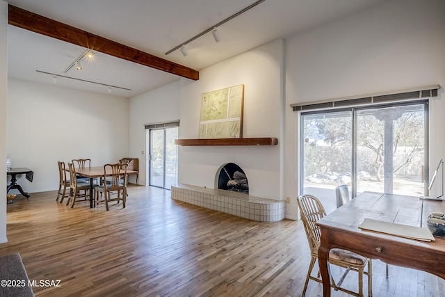 dining space with hardwood / wood-style flooring, rail lighting, beam ceiling, and a healthy amount of sunlight