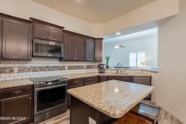 kitchen featuring sink, appliances with stainless steel finishes, backsplash, dark brown cabinets, and a kitchen breakfast bar