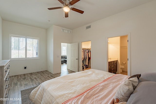 bedroom with ensuite bathroom, a spacious closet, light wood-type flooring, a closet, and ceiling fan