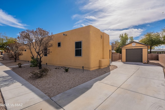 view of property exterior featuring a detached garage, concrete driveway, stucco siding, and fence