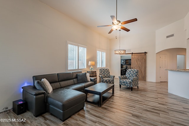 living room with light hardwood / wood-style floors, a barn door, ceiling fan, and a high ceiling