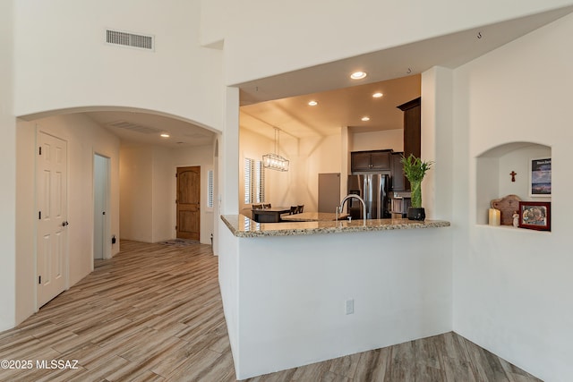 kitchen featuring visible vents, stainless steel fridge, dark brown cabinetry, and light wood finished floors