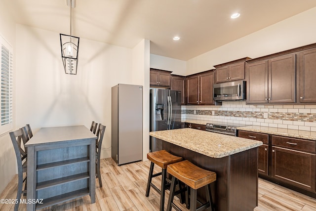 kitchen with decorative backsplash, dark brown cabinetry, light wood-style flooring, a kitchen island, and appliances with stainless steel finishes