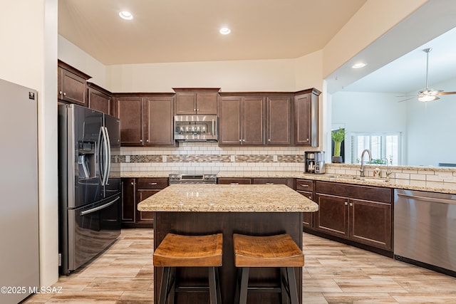 kitchen featuring tasteful backsplash, a sink, stainless steel appliances, dark brown cabinets, and a kitchen island
