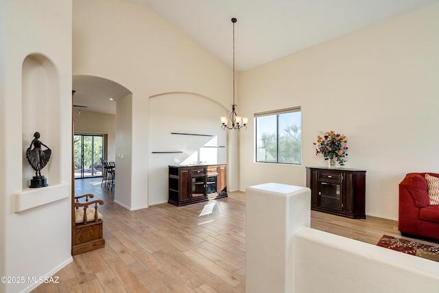 living room featuring high vaulted ceiling, an inviting chandelier, and light hardwood / wood-style floors