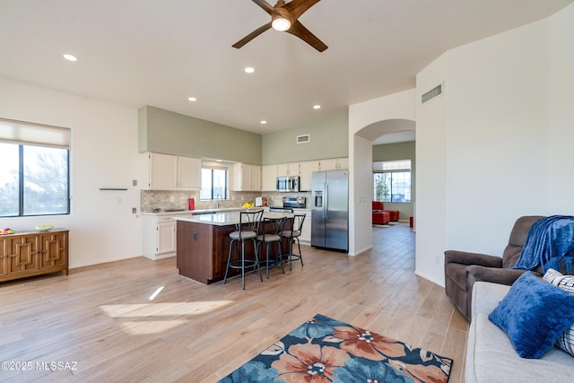 kitchen with white cabinets, appliances with stainless steel finishes, a kitchen island, a kitchen bar, and light hardwood / wood-style flooring