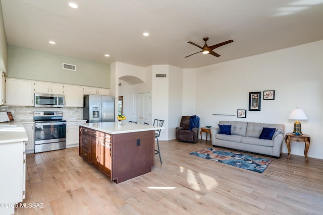 kitchen featuring appliances with stainless steel finishes, white cabinetry, a kitchen island, backsplash, and ceiling fan