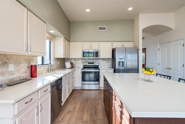 kitchen featuring white cabinets, appliances with stainless steel finishes, a kitchen island, tasteful backsplash, and sink