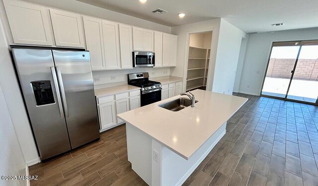 kitchen with white cabinets, a sink, a center island with sink, wood finish floors, and appliances with stainless steel finishes