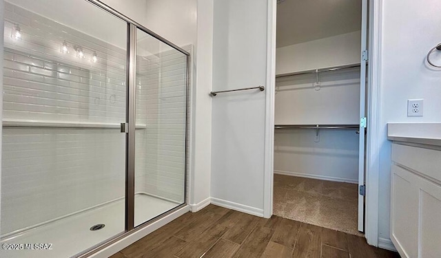 bathroom featuring a walk in closet, a shower stall, and wood finished floors