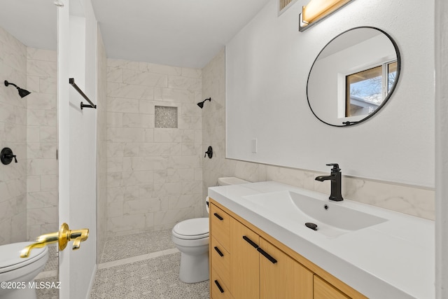 bathroom featuring vanity, toilet, tile walls, and a tile shower