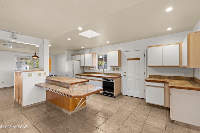 kitchen with a skylight, white cabinetry, sink, white refrigerator, and kitchen peninsula