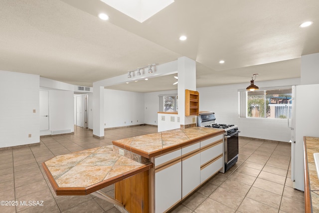 kitchen with light tile patterned flooring, tile countertops, range with gas cooktop, white cabinetry, and white refrigerator