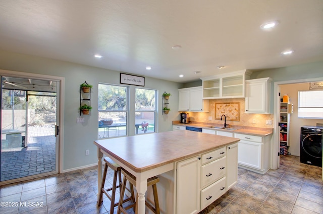 kitchen with a kitchen island, white cabinetry, washer / dryer, and sink