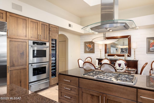 kitchen with stainless steel appliances, island exhaust hood, decorative light fixtures, and dark stone counters